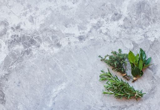 An overhead shot of bunches of rosemary, thyme and bay leaves on gray marble background with space for your text