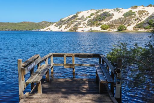 A natural view of a wooden dock over a calm lake against mountain and clear sky