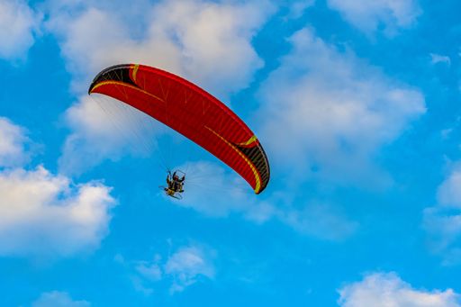 Red dome of a motor paraglider flying on a background of blue cloudy summer sky. Tandem on a paraglider high in the sky.