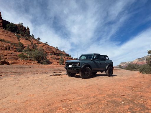 A beautiful dark green Ford Bronco parked on Sedona red rocks with cliff under cloudy sky