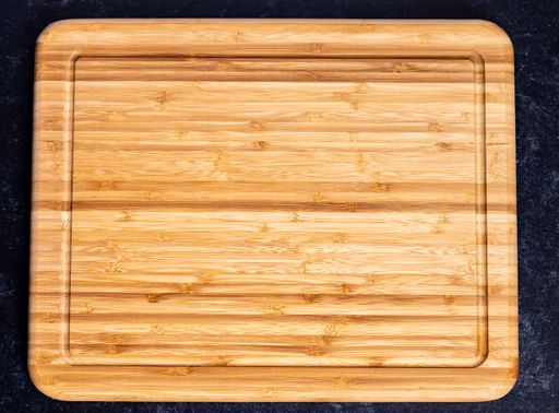 The top view of a rectangular wooden chopping board on the dark-colored surface
