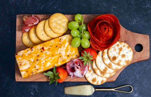 The top view of cheese, grapes, and strawberries on the wooden chopping board