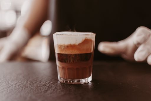 An individual is pouring freshly brewed coffee from a carafe into a glass cup, with a light background behind them