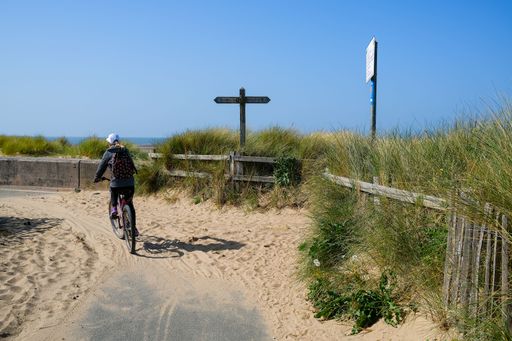 A young girl riding a bicycle on a sandy road on a coastal cycleway on a sunny day