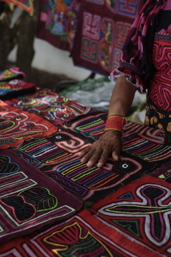 A vertical closeup of a Hispanic woman touching colorful mola fabric