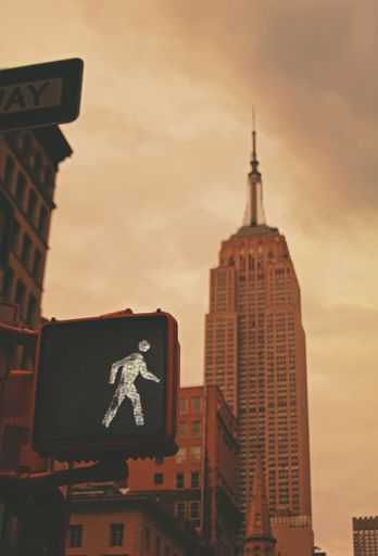 A vertical shot of a traffic sign for crossing with the Empire State Building in the background