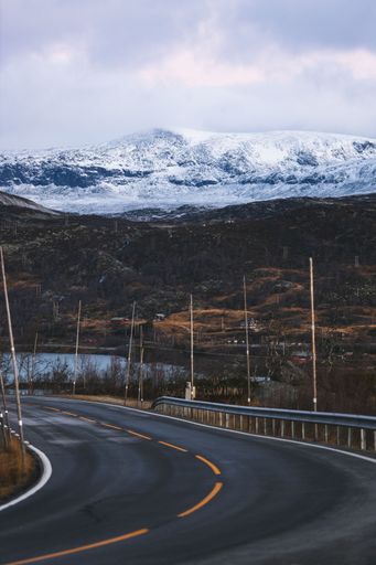A vertical shot of the rural road passing by the snowy mountains.
