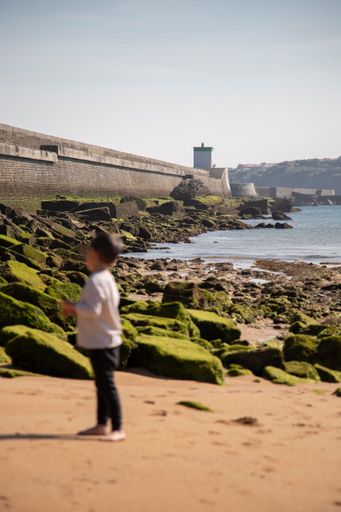 A vertical shot of the kid standing on the rocky beach in Port Socoa in France