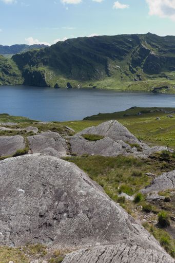 A vertical shot of beautiful scenery of a small lake in the middle of green and rocky hills, Ireland, UK