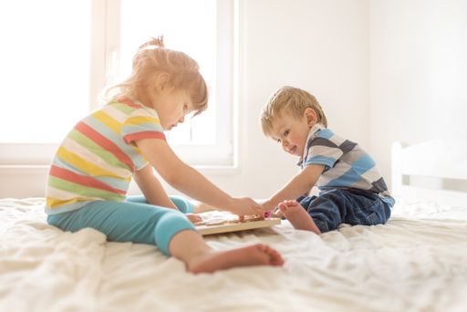 A brother and a sister playing on the bed in the bedroom