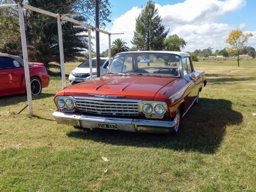 Old popular maroon Chevrolet Chevy Impala four door sedan 1960s in countryside. Front view. Grill. Nature, grass, trees. Classic car show. Copyspace