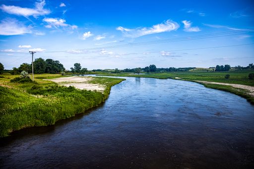 An aerial view of flowing river surrounded by greenery fields under blue bright sky