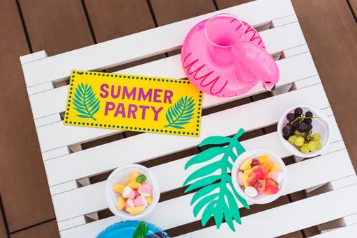 A high angle shot of sweet snacks and inflatable pool cup holders with the tag "SUMMER PARTY" on a white wooden stool