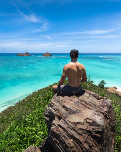A vertical shot of the back of a half-naked male sitting on a rock on the shore in Lanikai, Oahu Hawaii