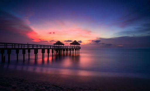 A scenic evening view of a pier over a body of water reflecting the colorful sky