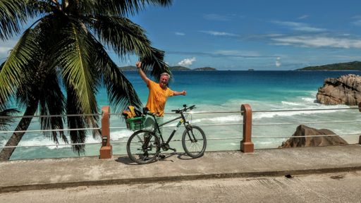 A closeup of a male Caucasian leaning on the coastal barrier with his bicycle in La Digue, Seychelles