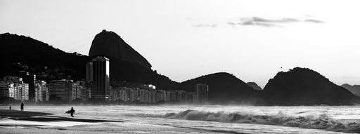 A panoramic grayscale shot of Copacabana beach in Rio de Janeiro with the Sugarloaf mountain on the background