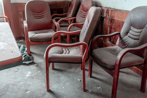 A closeup of red office chairs around a dusty table in an abandoned building