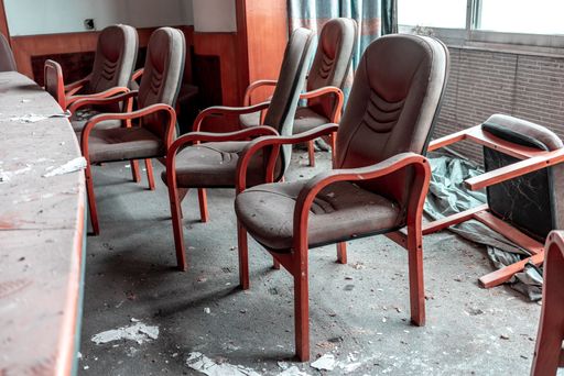 A closeup of red office chairs around a dusty table in an abandoned building