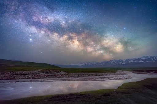 A scenic view of a starry night sky above a tranquil lake surrounded with beautiful mountains