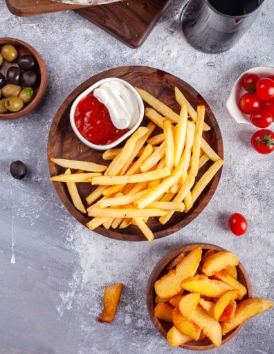 A vertical top view of French fries with ketchup and mayo and different ingredients on the side