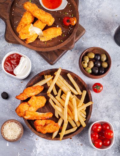 A vertical top view of French fries, crispy chicken and mozzarella sticks with various snacks on the side