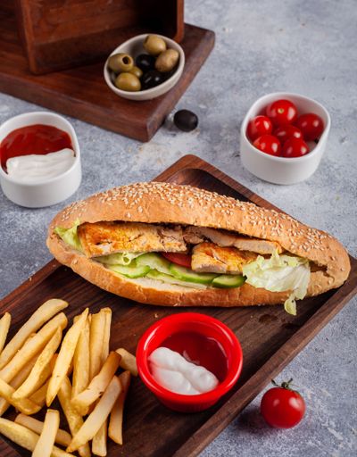 A vertical shot of a sandwich with french fries and sauces