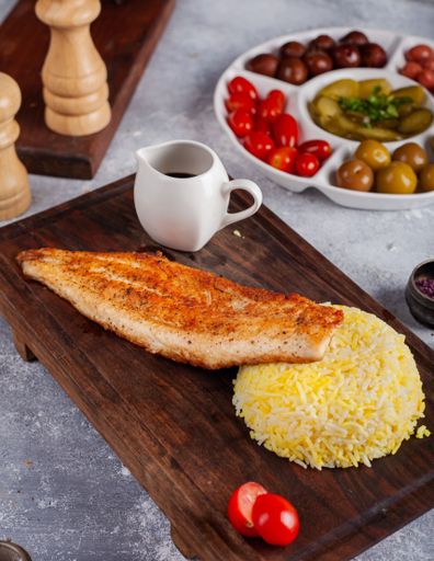 A vertical shot of a grilled fish with rice on a wooden board