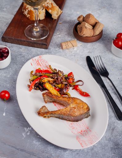 A vertical shot of a grilled salmon with vegetables on an oval plate