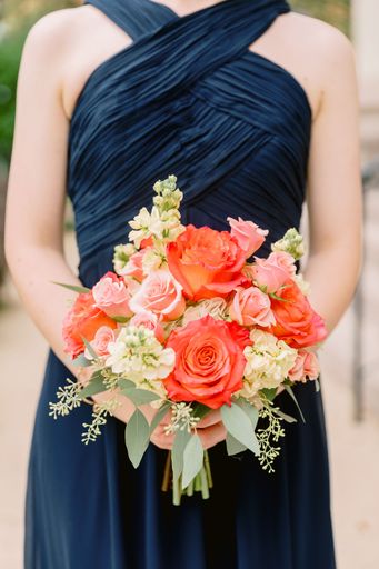A selective focus shot of the bridesmaid holding a red and pink bouquet