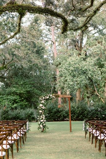 A scenic shot of a wedding venue in the park with wooden chairs under the trees