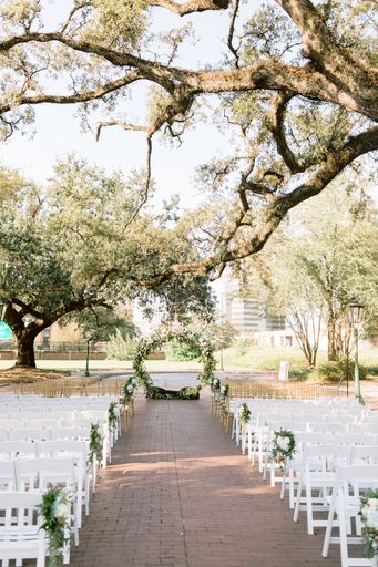 A scenic shot of a wedding venue in the park with white chairs and a flowery arch