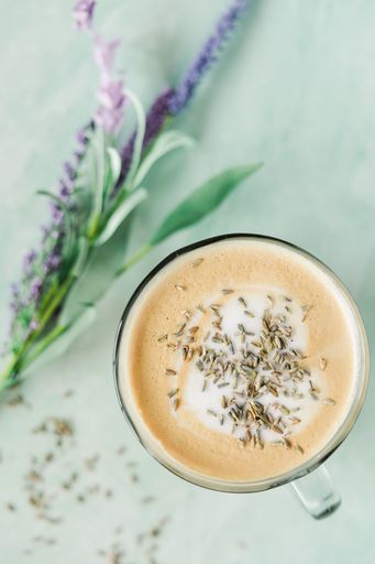 A top view shot of a cappuccino coffee drink with a lavender branch next to it on a turquoise board