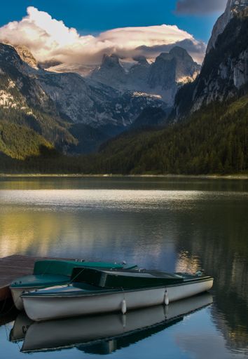 Two fishing boats near a pier in a lake surrounded by scenic mountains at sunset