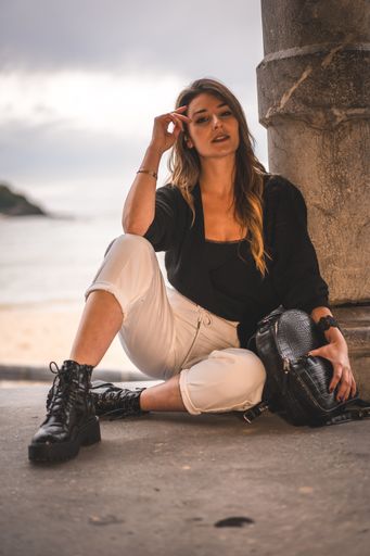 A shallow focus of a young attractive female with long hair sitting on the ground of a building surrounded by the sea
