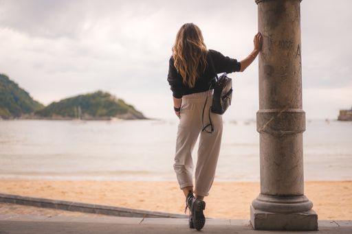 A shallow focus of a young female with long hair leaning on a column of a building surrounded by the sea