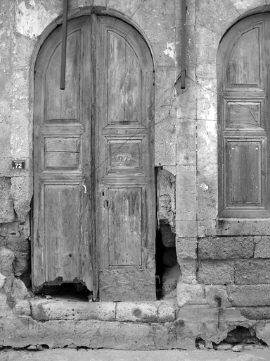 A vertical greyscale shot of a weathered wooden door of an old building in Alacati, Turkey