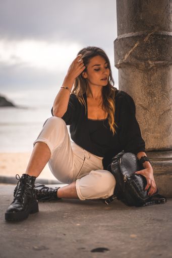 A shallow focus of a young attractive female with long hair sitting on the ground of a building surrounded by the sea
