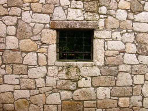 An old stone wall with a small barred window in Alacati, Izmir, Turkey