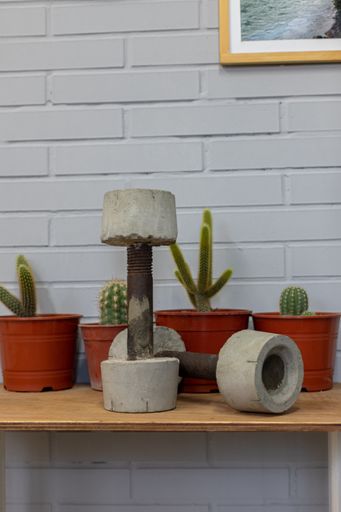 A closeup of weathered concrete dumbbells on a wooden surface with cacti in the back