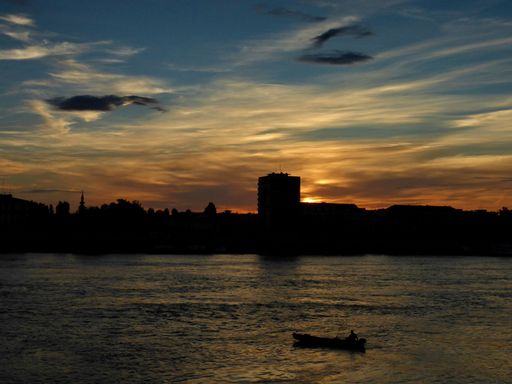 City skyline silhouette at sunset by the river with fisherman in the boat