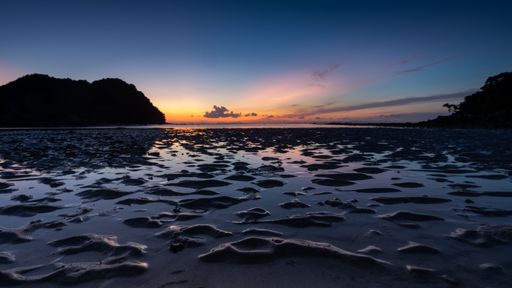 A beautiful shot of water in the middle of rocks with the silhouette of mountains in the distance at sunset