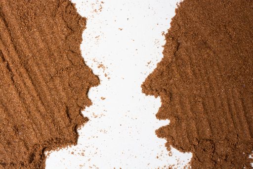 An overhead shot of faces facing each other made of ground coffee on a white surface