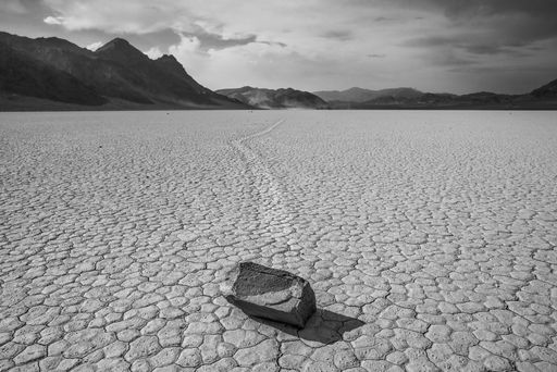 A horizontal greyscale shot of stone at the end of a trace surrounded by high rocky hills in Death Valley, USA