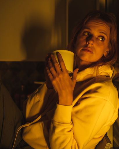 A vertical closeup of a beautiful woman looking out of the window, holding a mug.