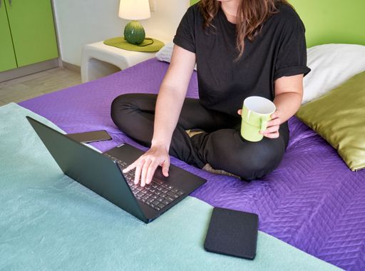 A female working from home by a laptop with a mug in a hand