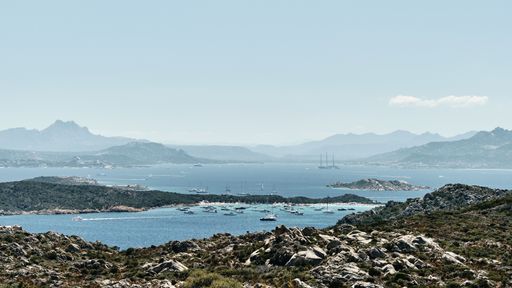 A wide shot of a grassy hill with rocks near the sea under a blue sky at daytime