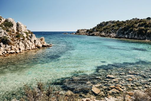 A beautiful shot of the sea near rocks and grassy hills under a blue sky at daytime