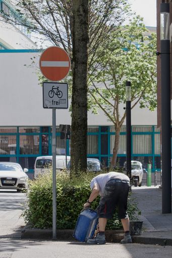 A vertical of a man working on the street near a passage with forbidden sign
