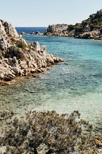 A vertical shot of the sea near rocky cliffs with a blue sky in the background at daytime
